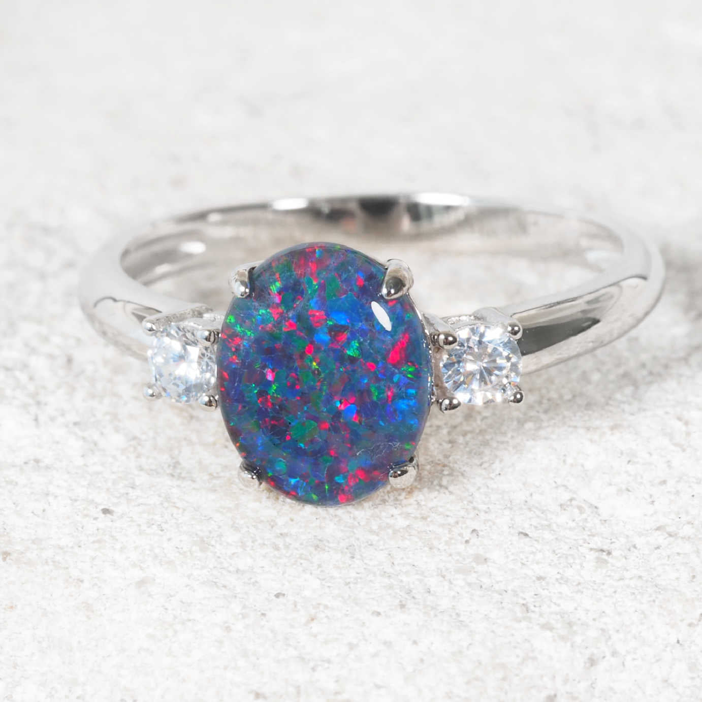 Silver ring with a colorful opal stone on a textured white background