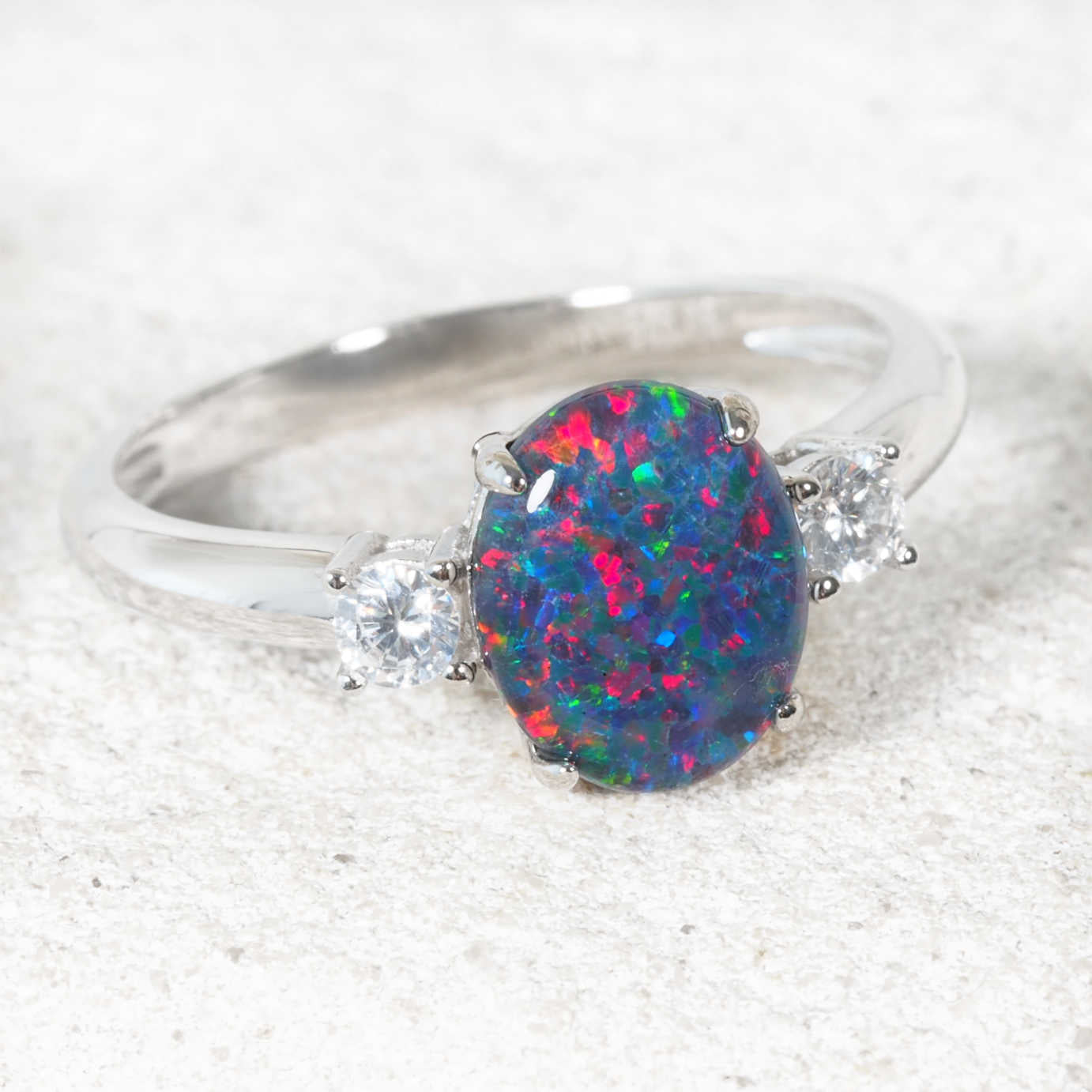 Silver ring with a colorful opal stone and two smaller crystals on a textured white surface