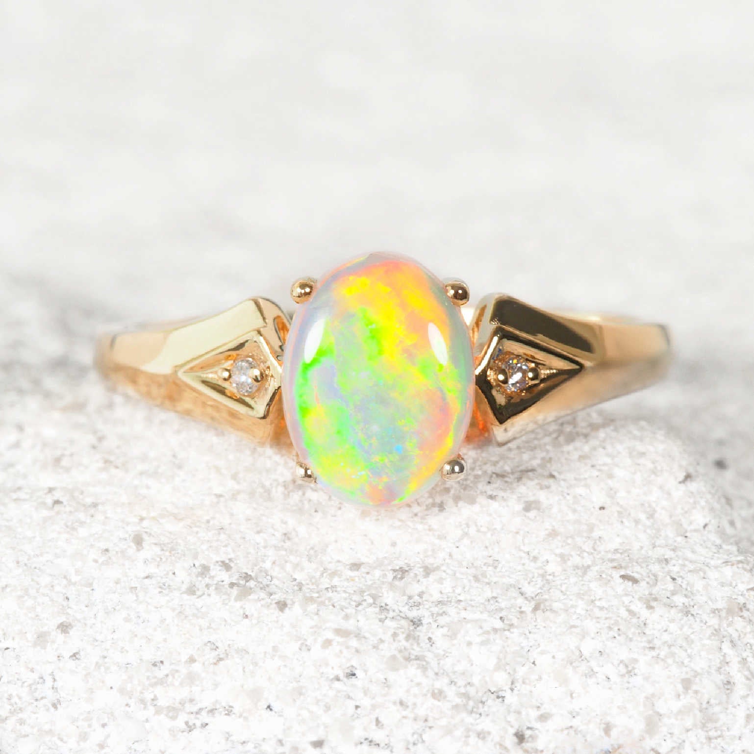 Gold ring with a colorful opal stone on a light gray background