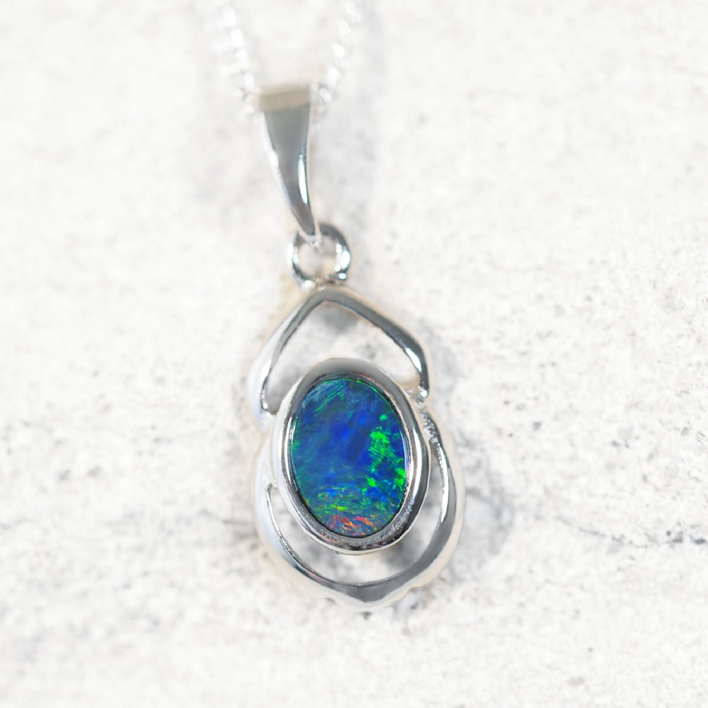Silver pendant with a colorful opal gemstone on a textured white background