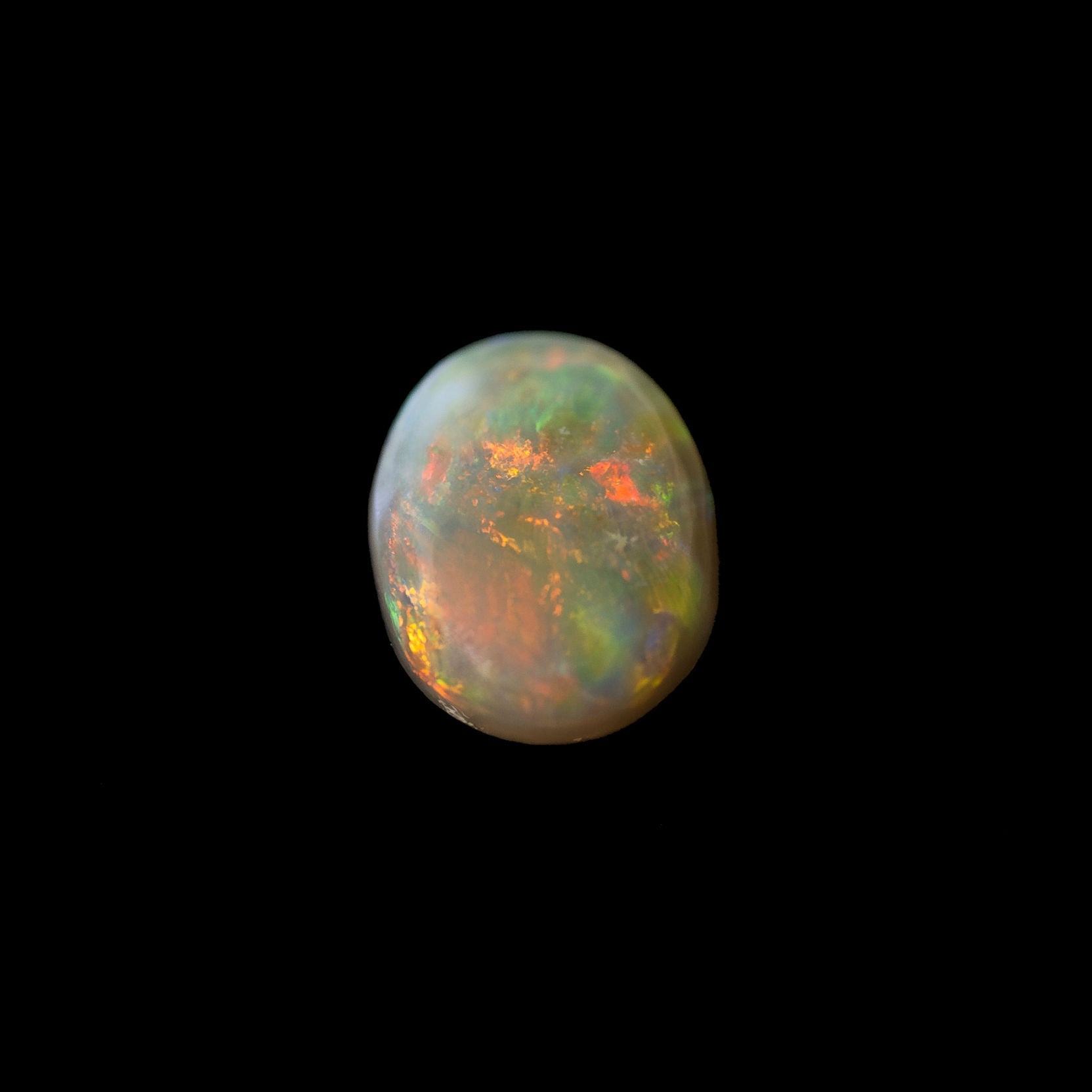 Close-up of natural black opal showing strong red flash with green and gold tones