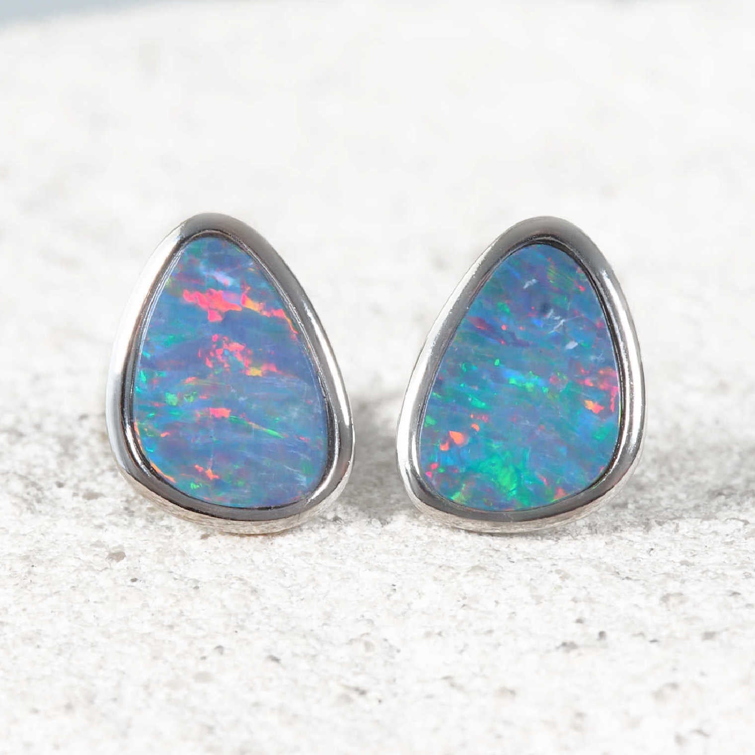 Teardrop-shaped opal earrings on a textured white surface