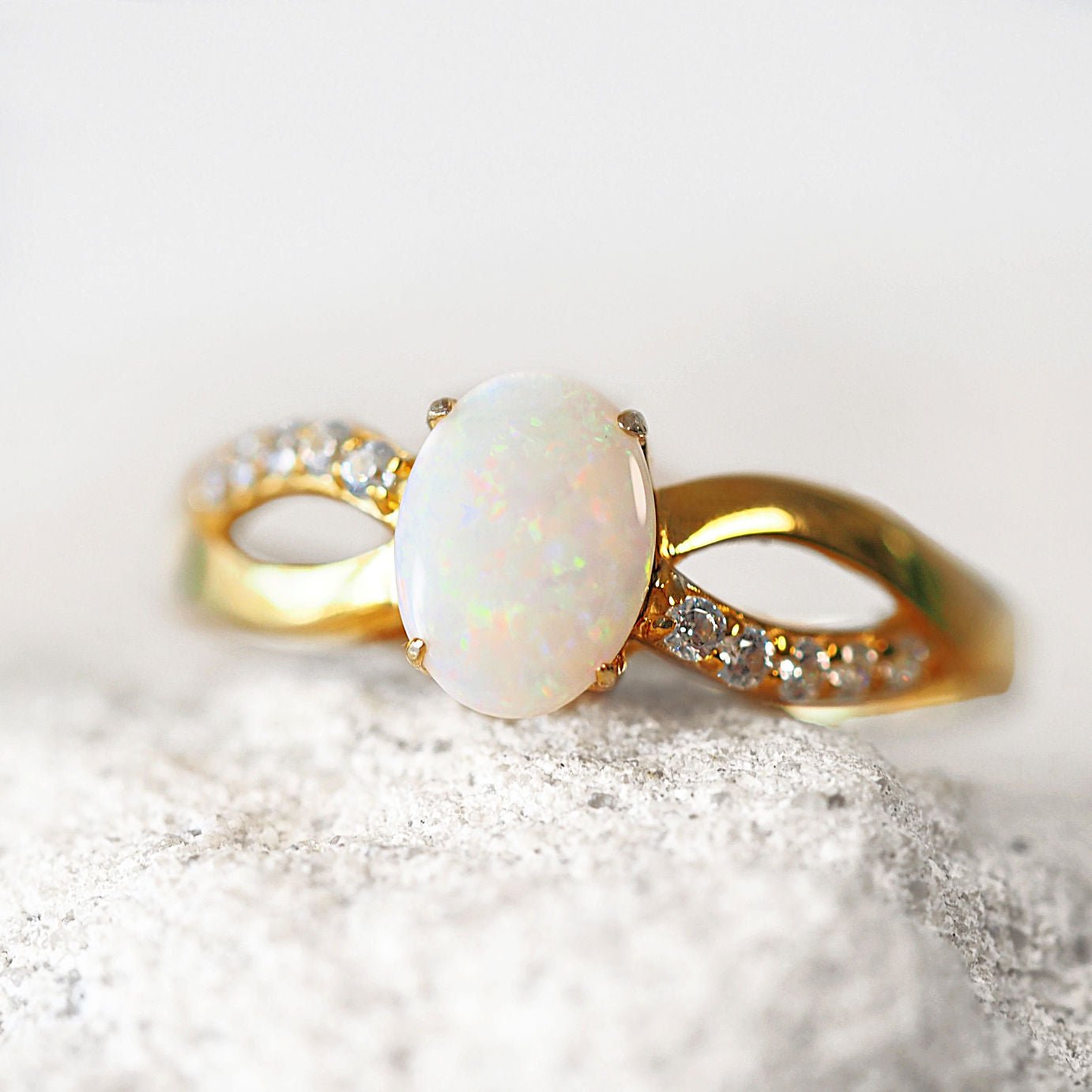 Gold ring with a large white opal gemstone and smaller clear stones on a textured surface