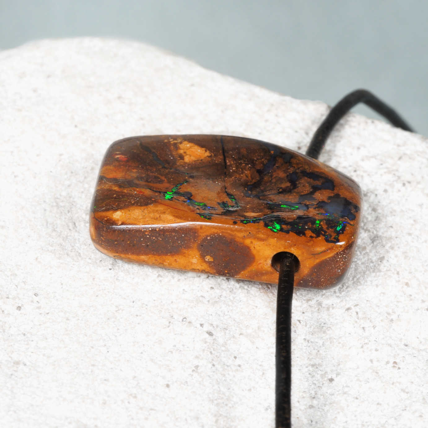 Boulder opal pendant with embedded stones on a textured surface