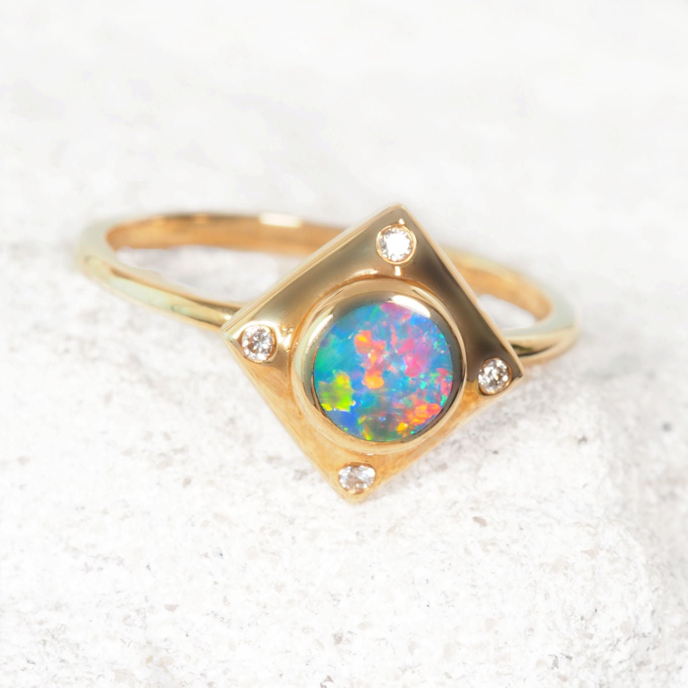 Gold ring with a colorful opal stone on a textured white surface