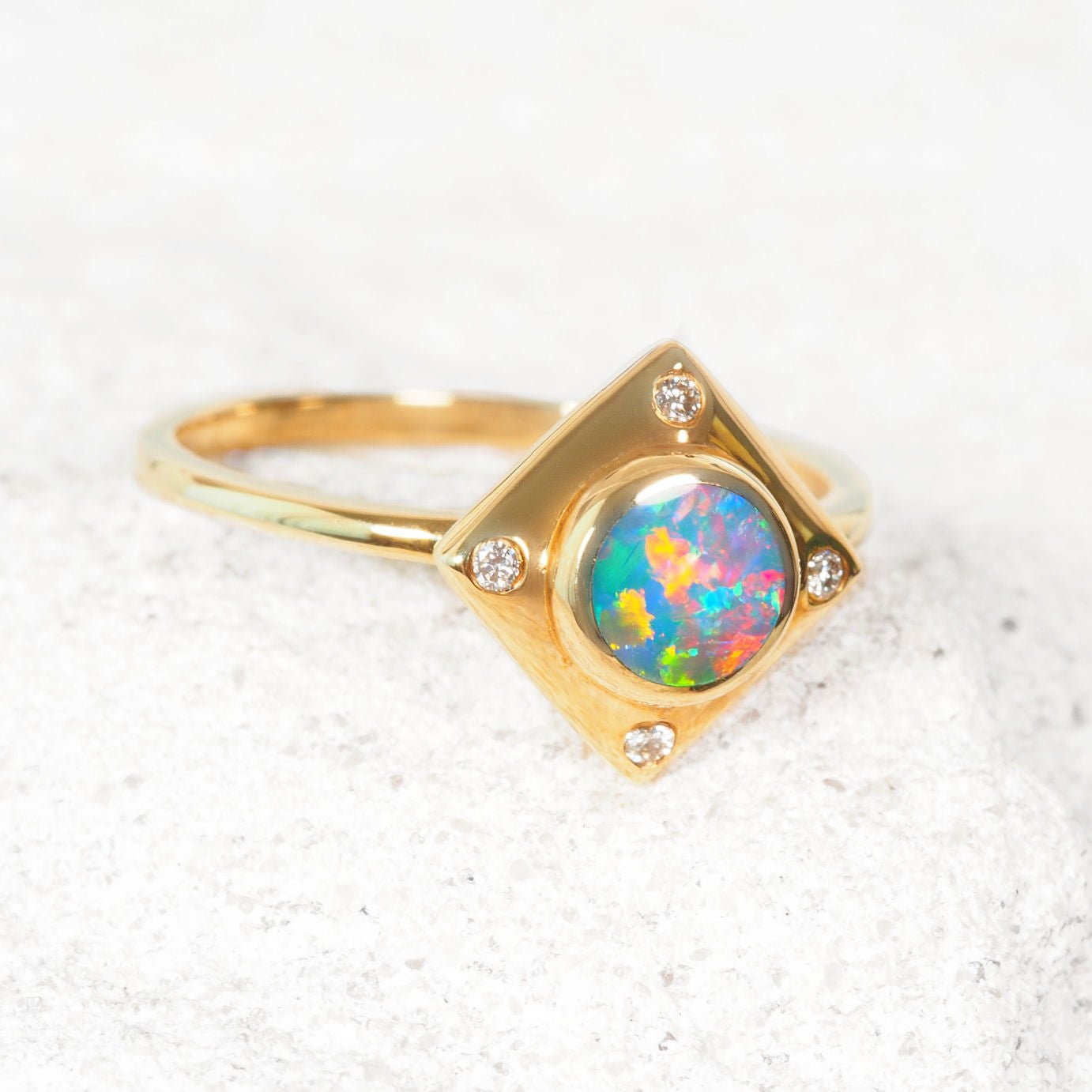 Gold ring with a colorful opal stone on a textured white surface