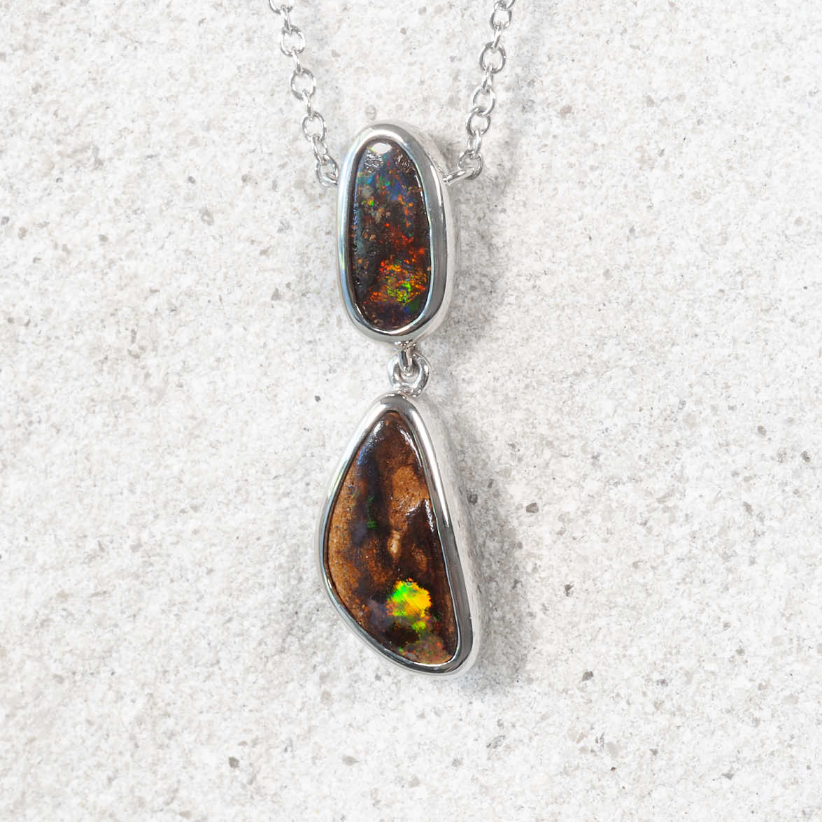 Silver pendant with two opal stones on a textured white background