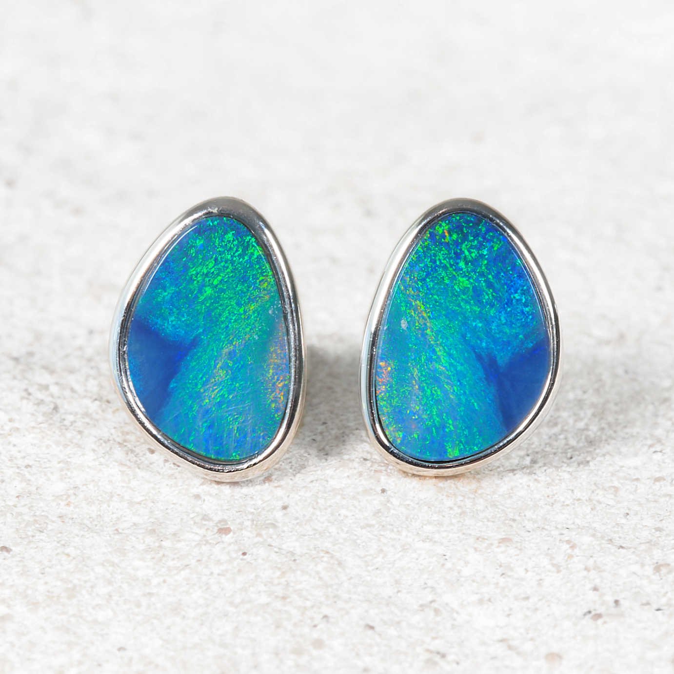 Pair of opal earrings with silver setting on a textured white surface