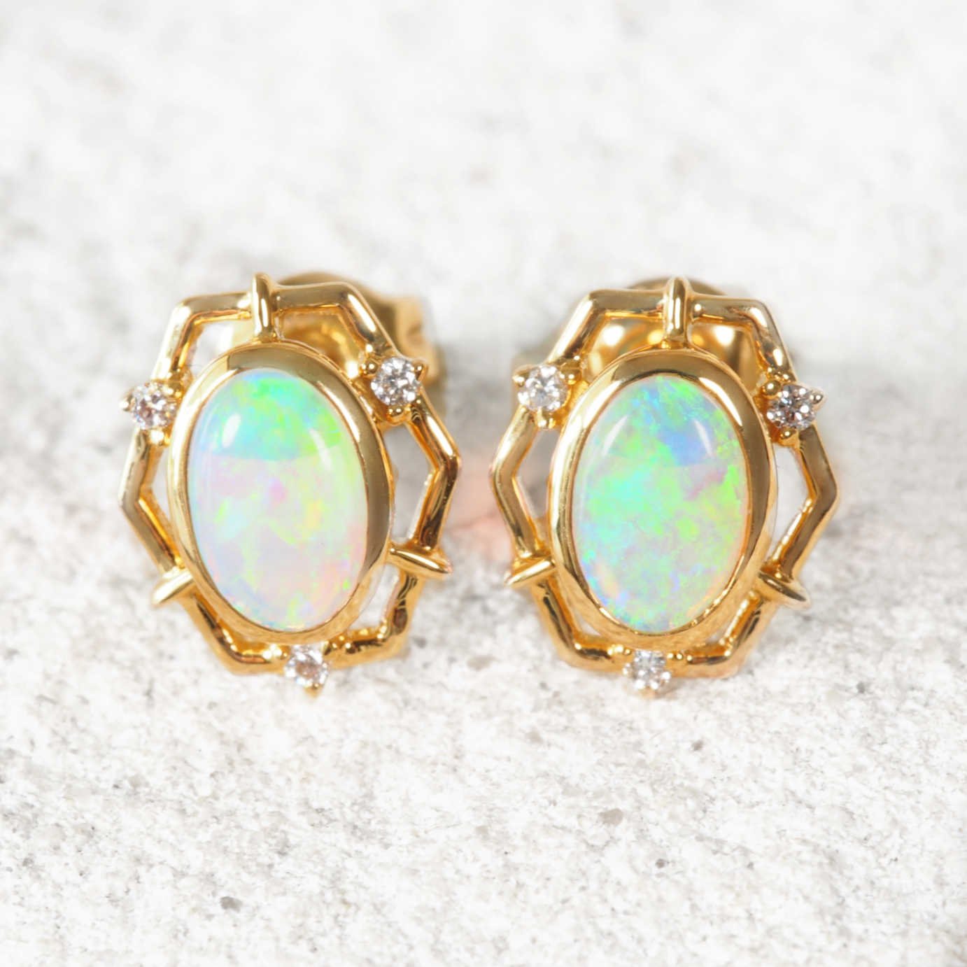 Pair of gold-framed opal earrings on a textured white surface