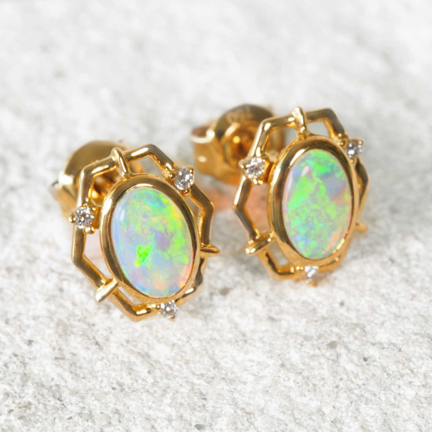 Gold earrings with opal stones on a textured white background