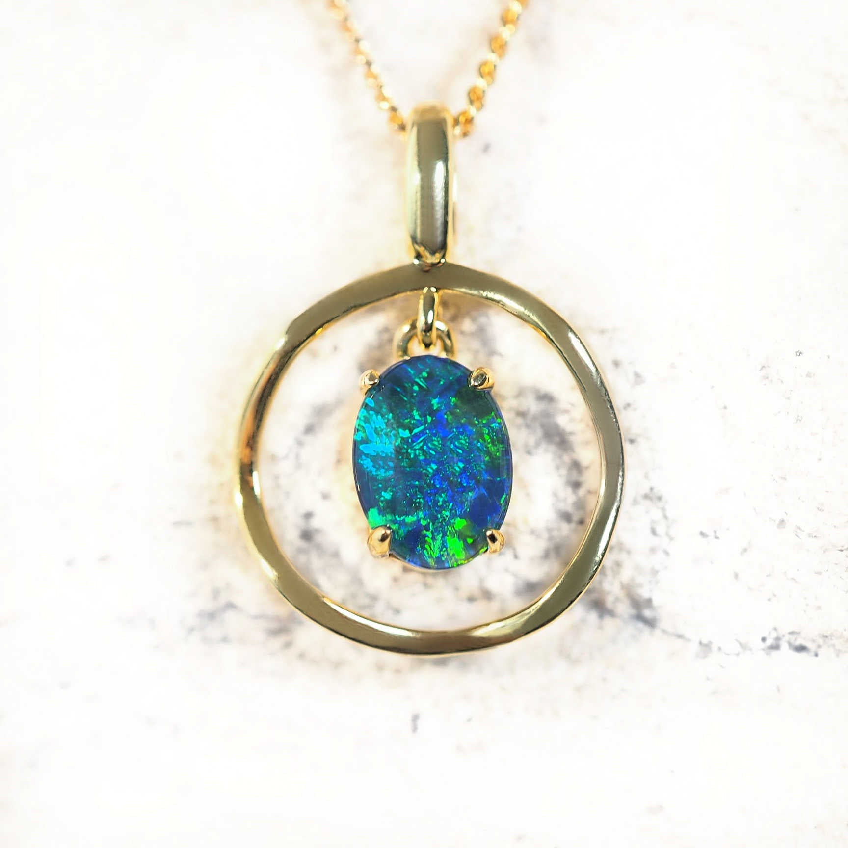 Gold-plated silver drop-style opal pendant necklace with claw-set blue and green Australian triplet opal framed in a double-layered circular design, shown with matching chain.