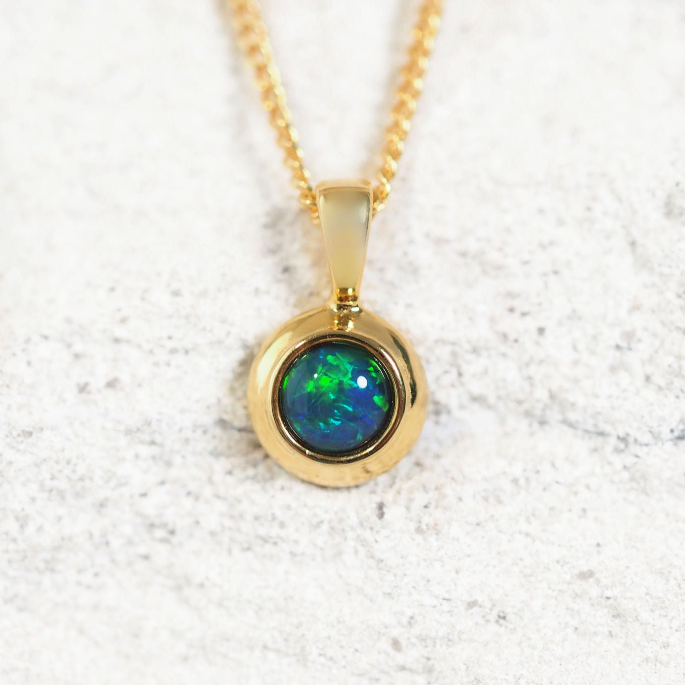 Gold plated silver opal pendant with a green and blue opal stone on a white background