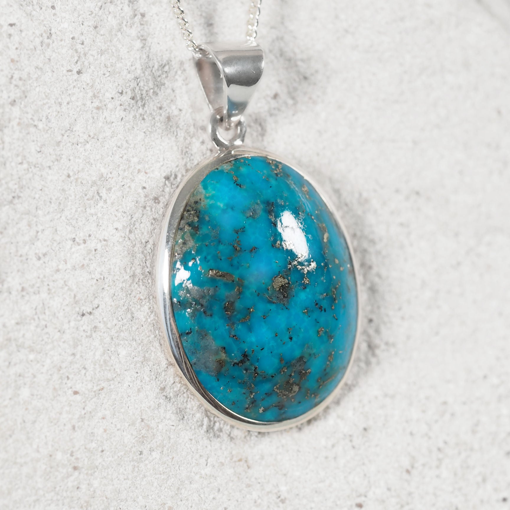 Turquoise stone pendant on a silver chain against a white background