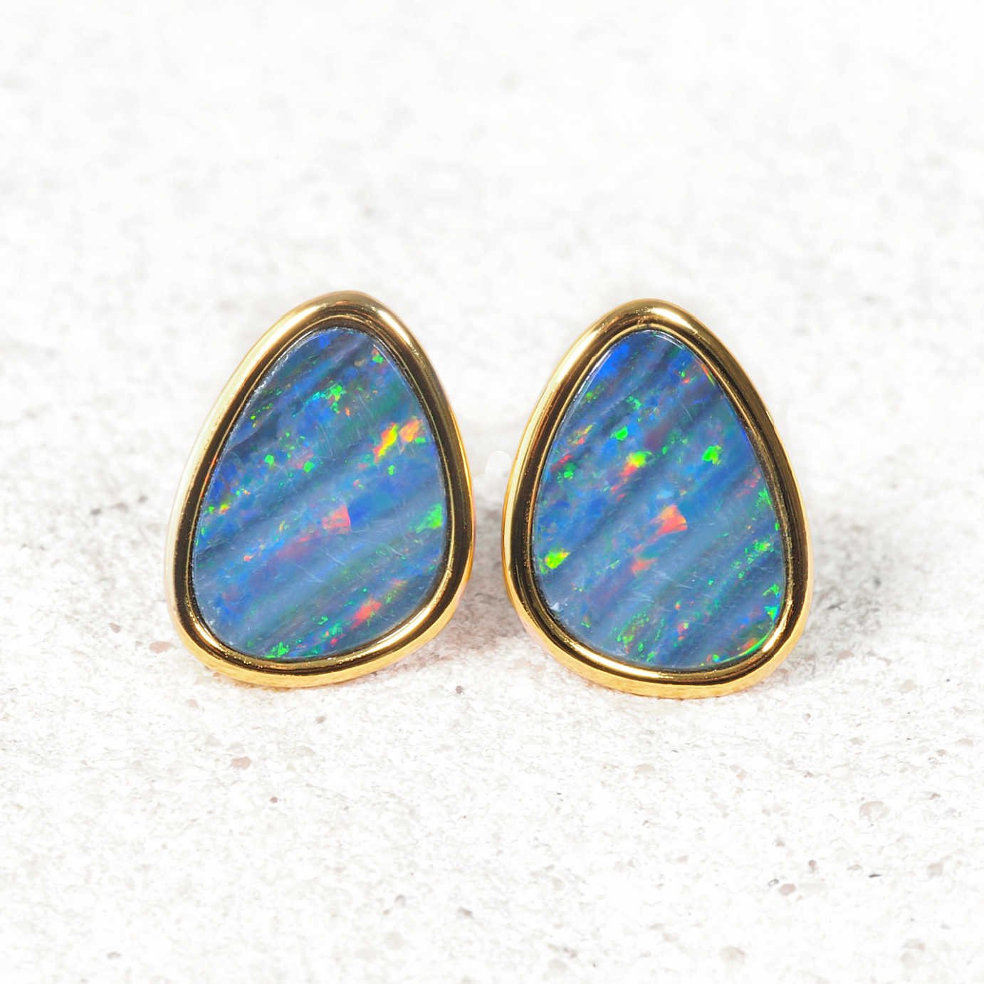 A pair of gold pear-shaped opal stud earrings with vibrant blue opal stones showing flashes of green, orange, and pink, set against a light textured background.