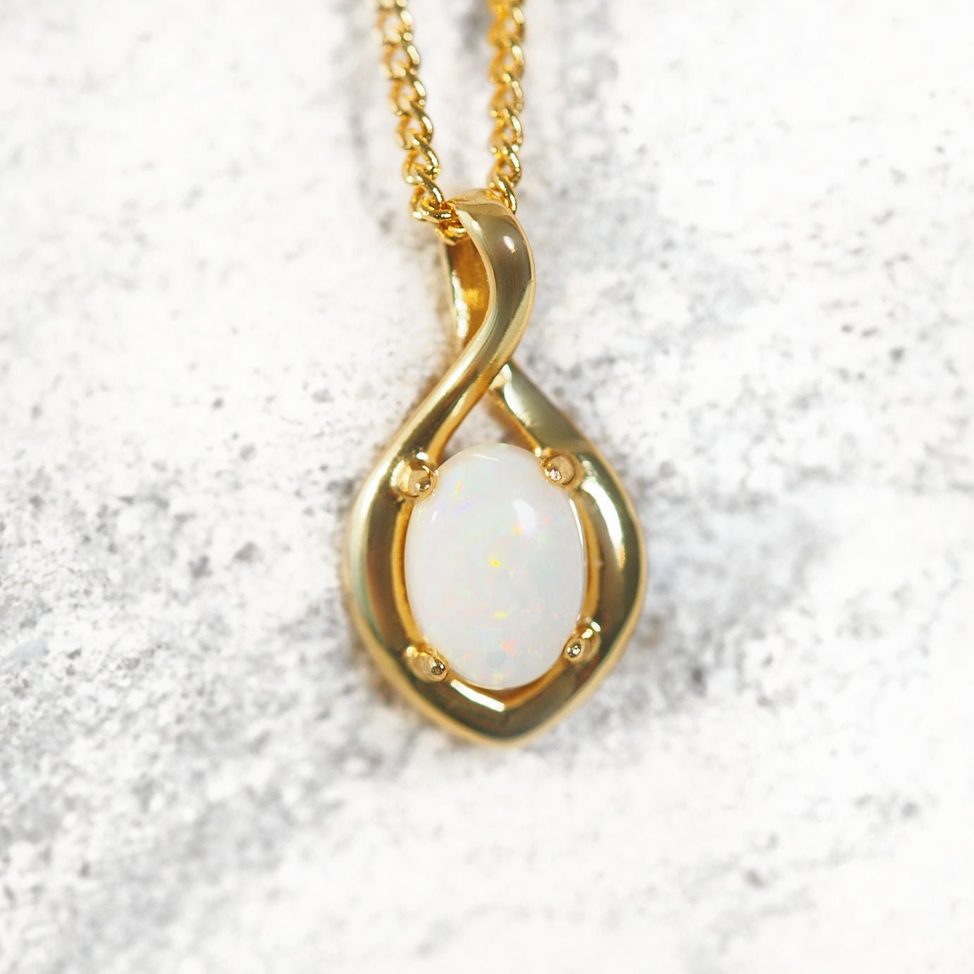 Gold opal pendant with a white stone on a textured white background