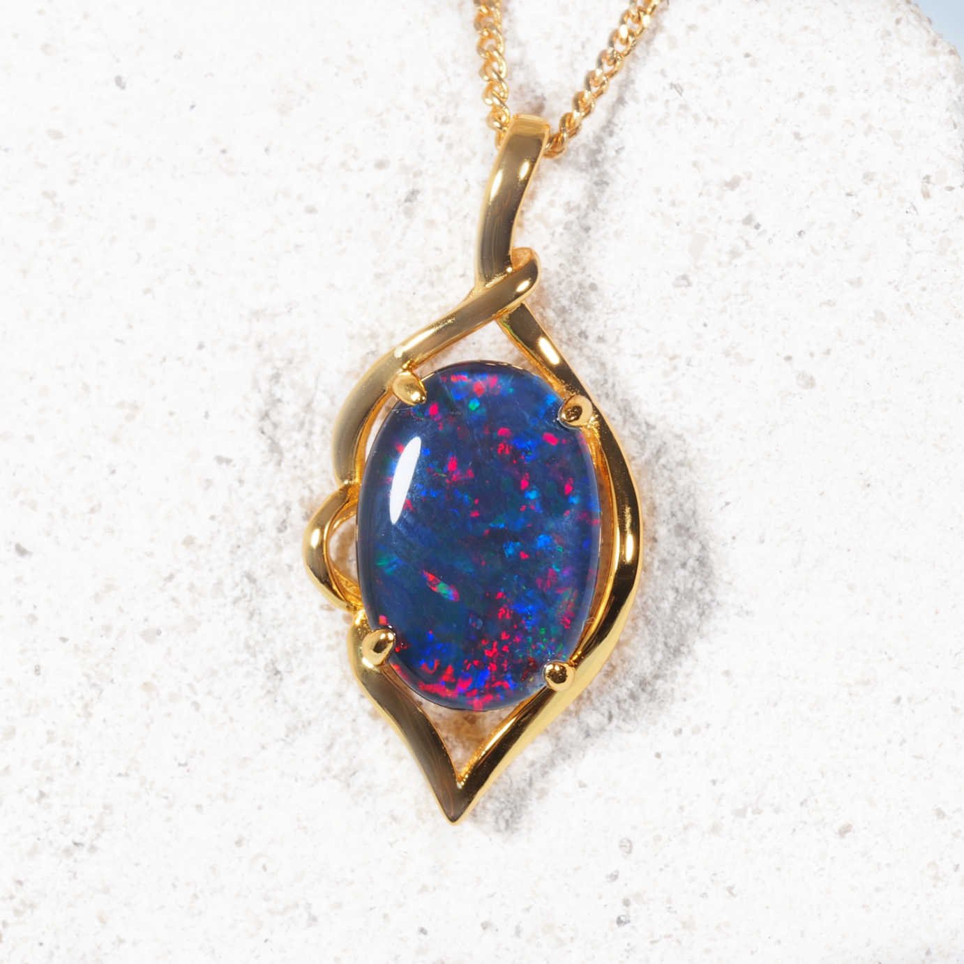 Gold opal pendant with a blue opal stone on a white sand background