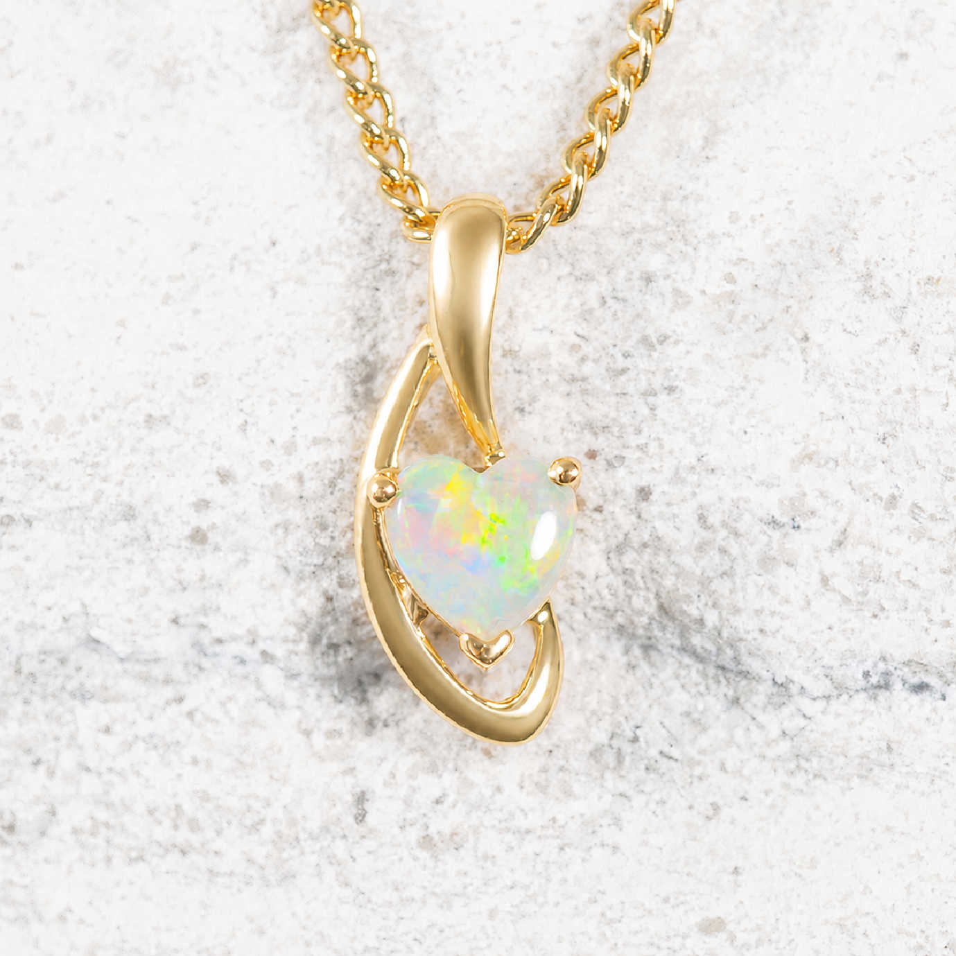 Gold necklace with a heart-shaped opal pendant on a textured white background