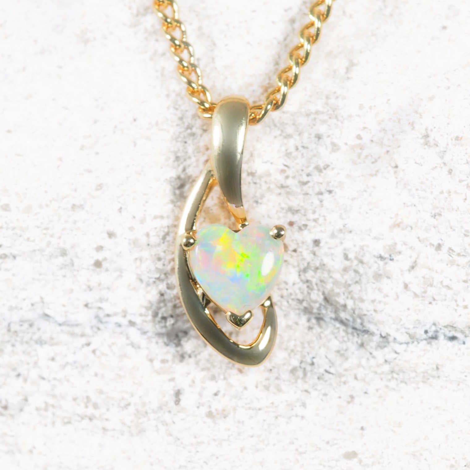 Gold necklace with a heart-shaped opal pendant on a textured white background