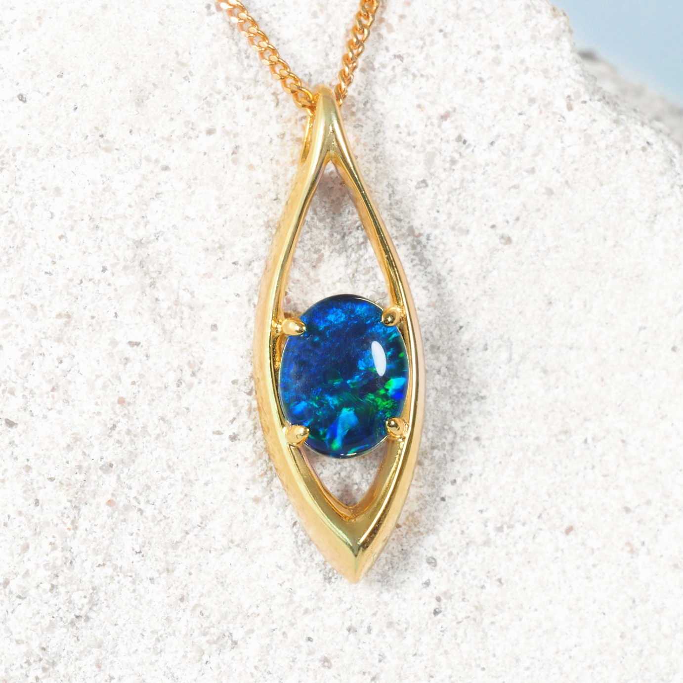 Gold plated silver opal pendant with a blue opal gemstone on a textured white surface