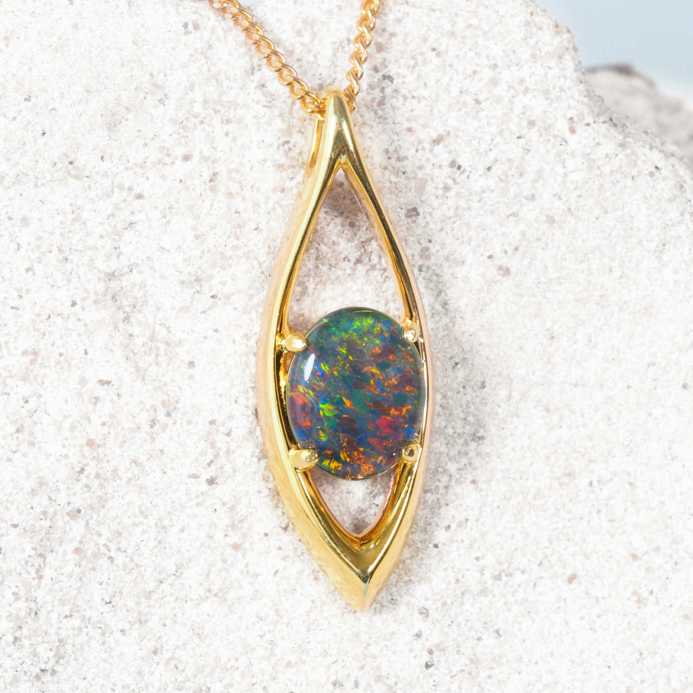 Gold pendant with a colorful opal stone on a textured white surface