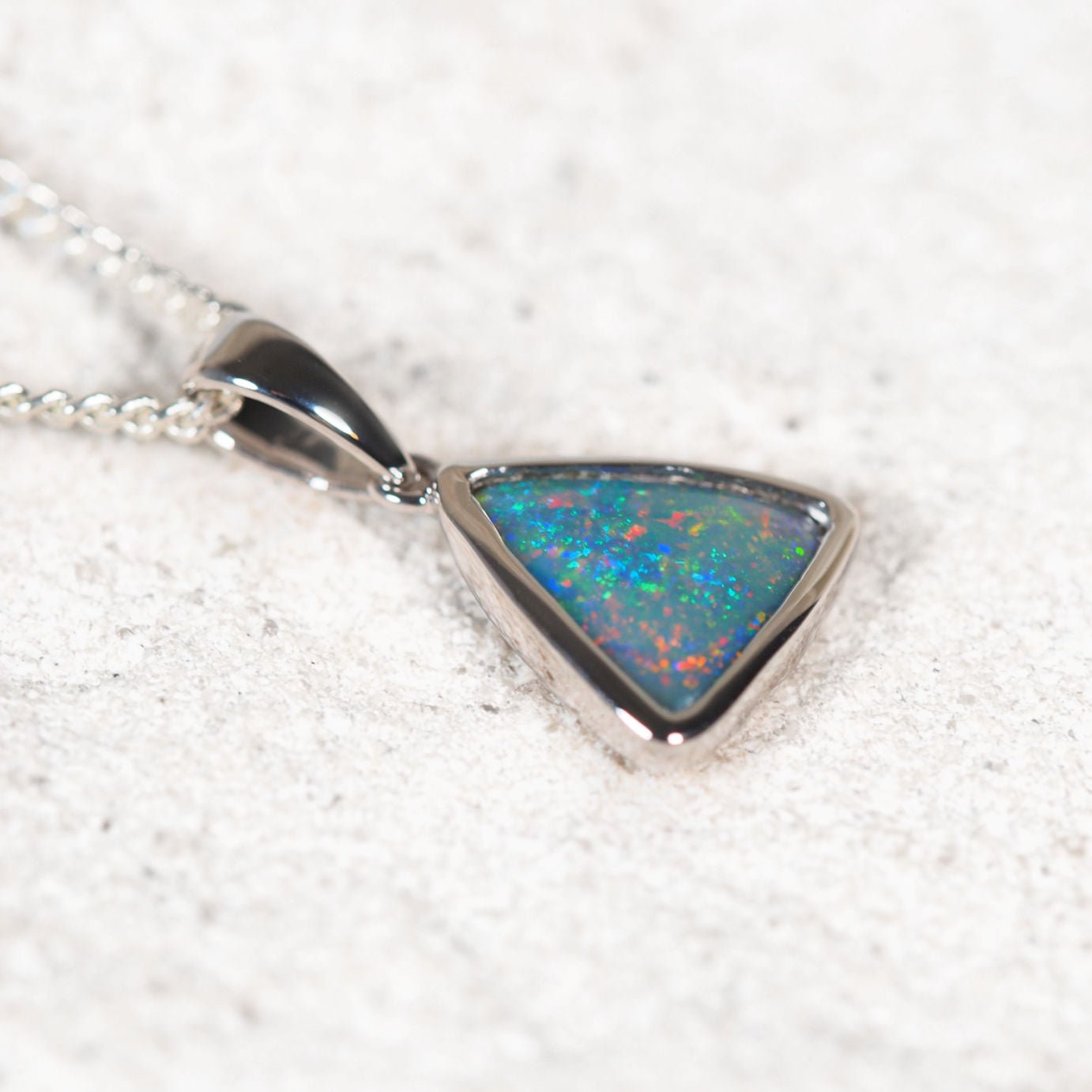 Triangular Lightning Ridge black opal pendant showing vivid pinfire flashes of red, green and blue in white gold setting