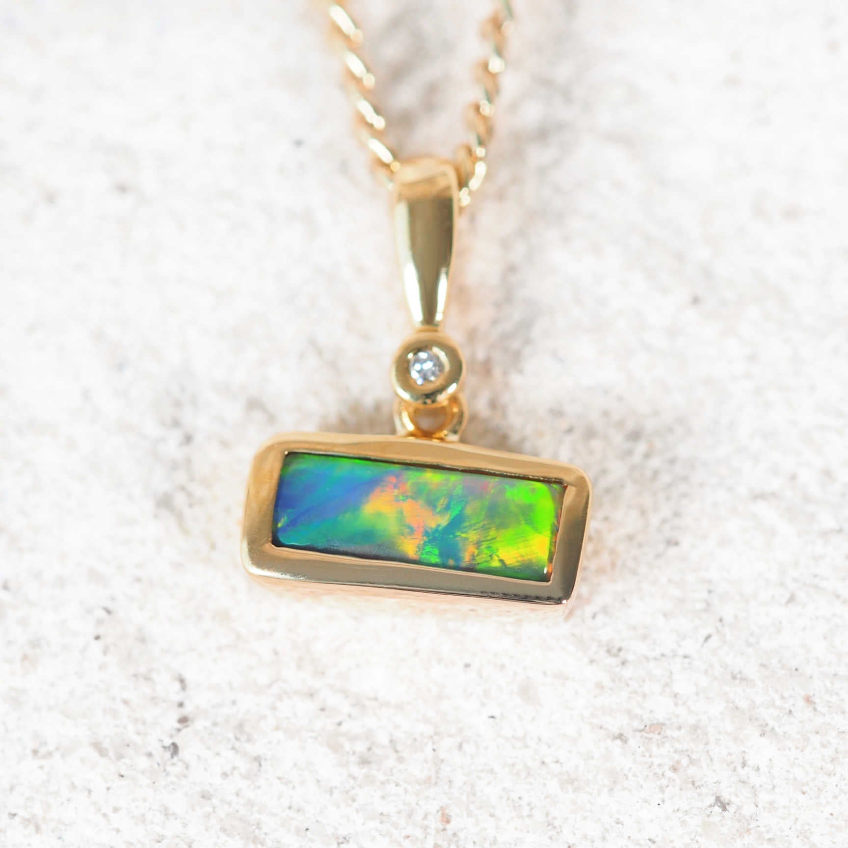 Elegant black opal and diamond pendant featuring vivid blues and greens in bezel setting