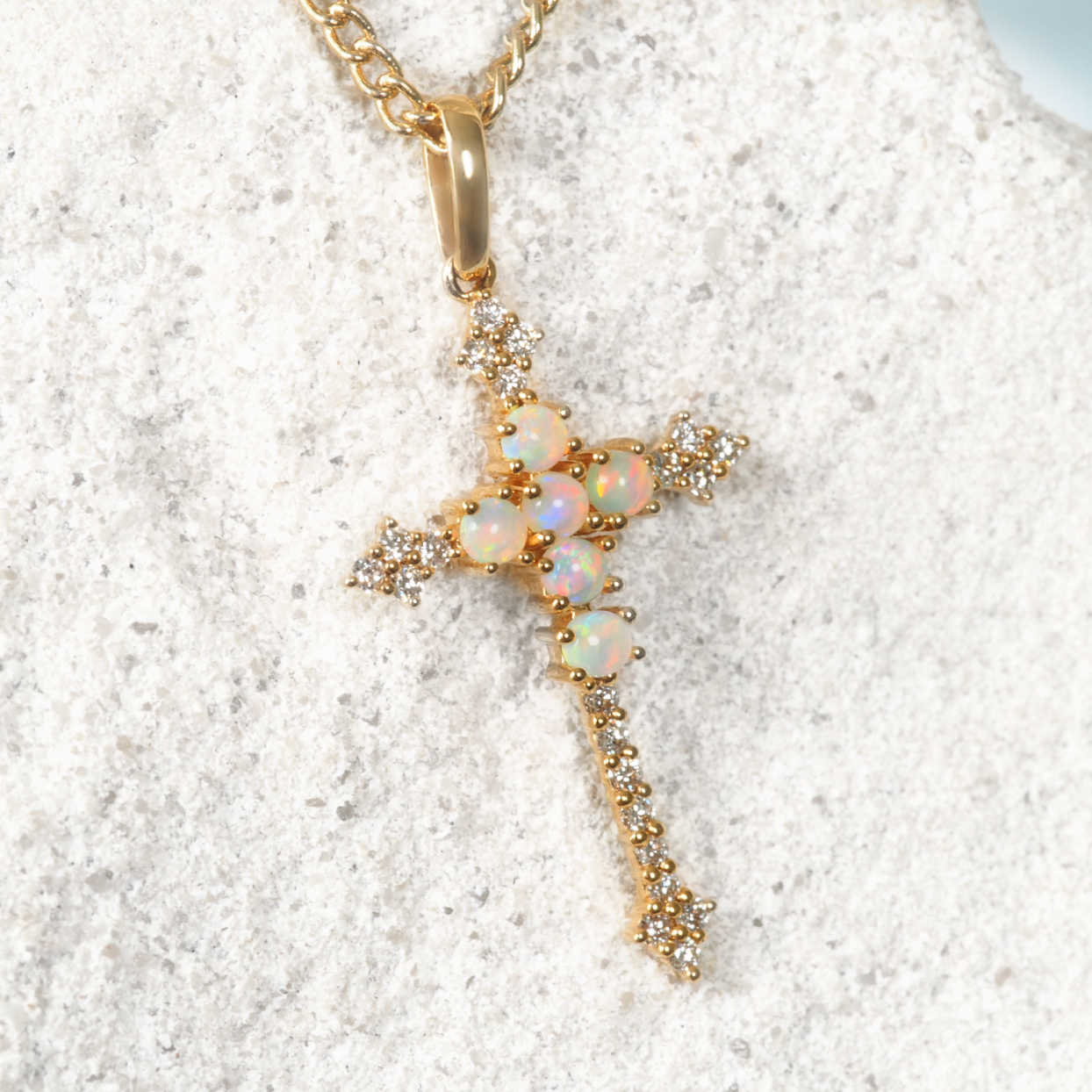Opal pendant on a gold chain against a white sand background