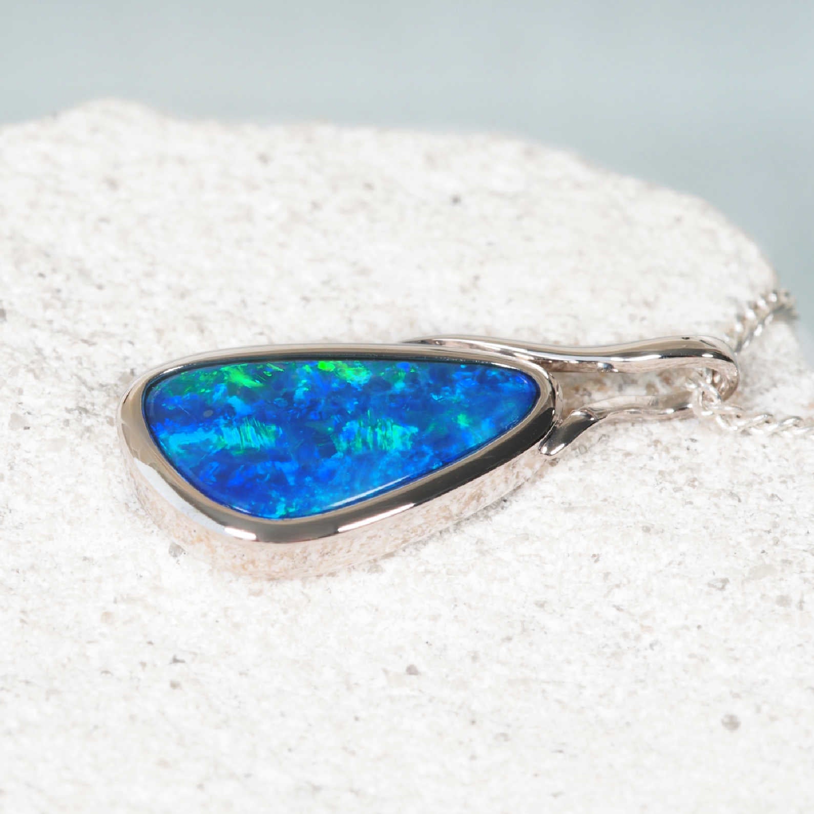 Blue and green opal pendant on a white sandy background