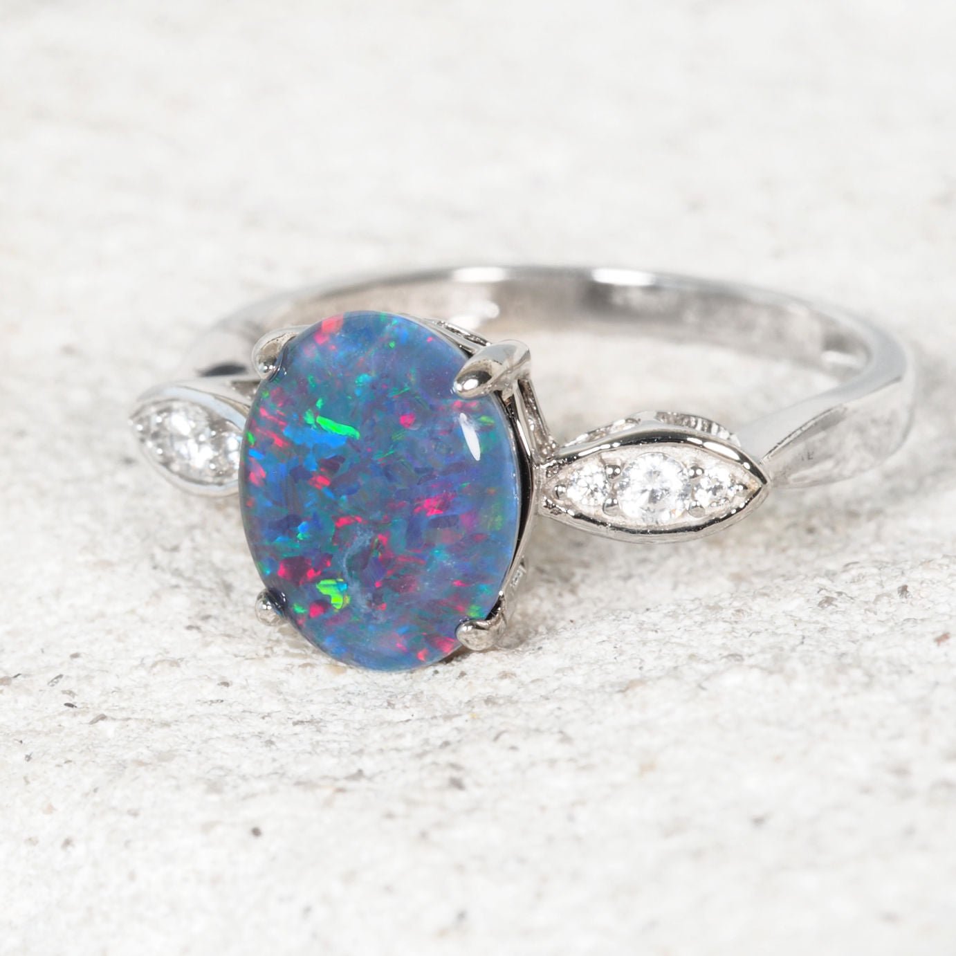 Ring with a colorful opal stone and diamond accents on a light background