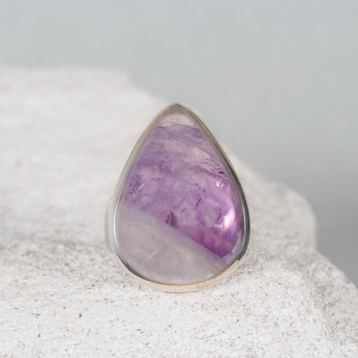 Elegant silver ring, ‘Mary,’ featuring a smooth teardrop triangular amethyst cabochon with mostly light purple tones.