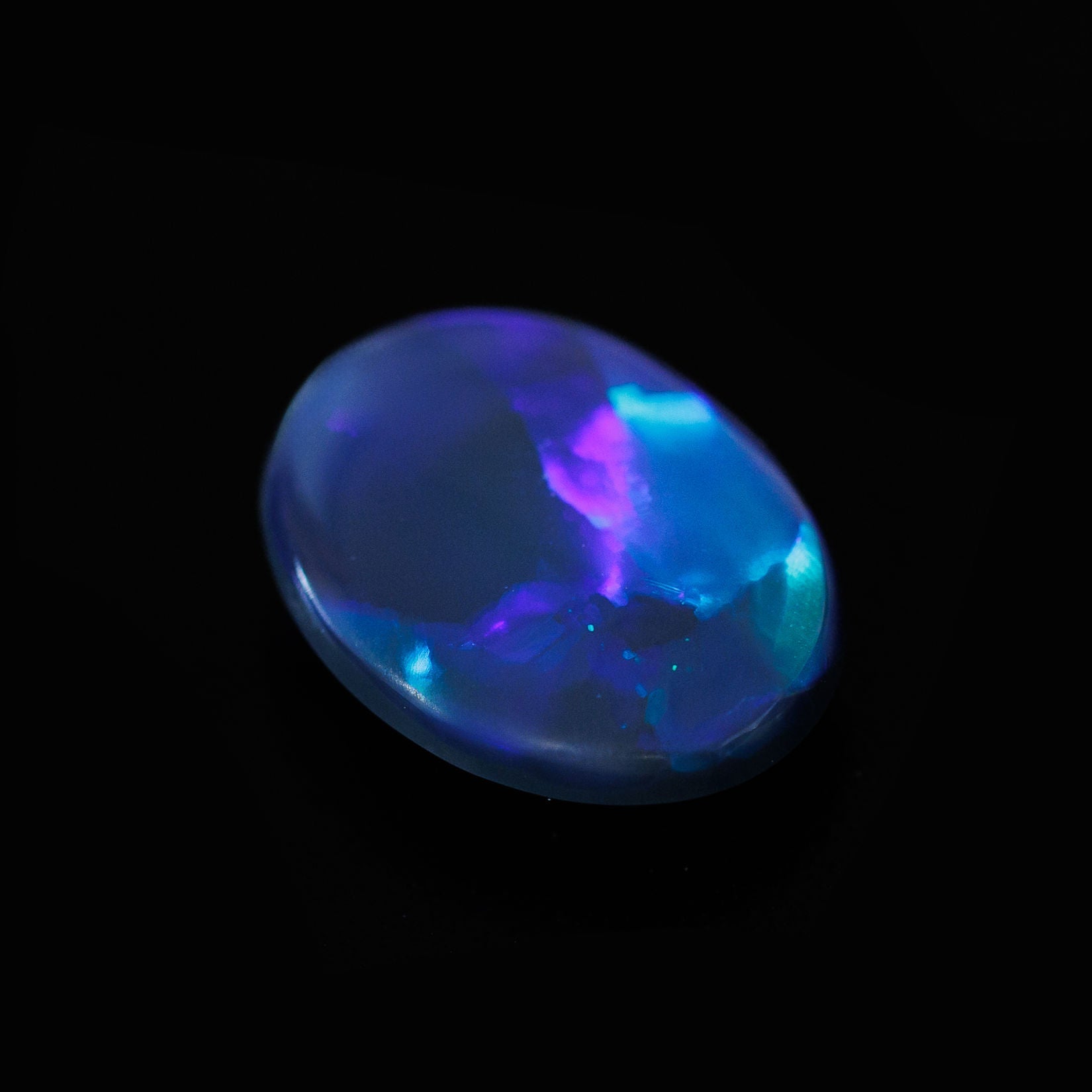 Natural solid Australian black opal featuring vibrant flashes of blue and green against a dark body tone