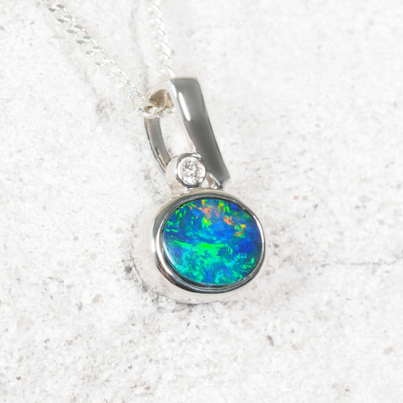 Australian opal pendant with white gold setting on a textured white background