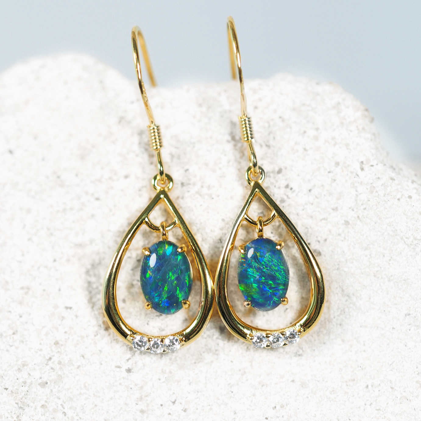 Gold earrings with opal stones on a white stone background