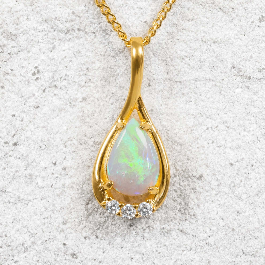 Gold pendant with opal stone and small diamonds on a textured white background