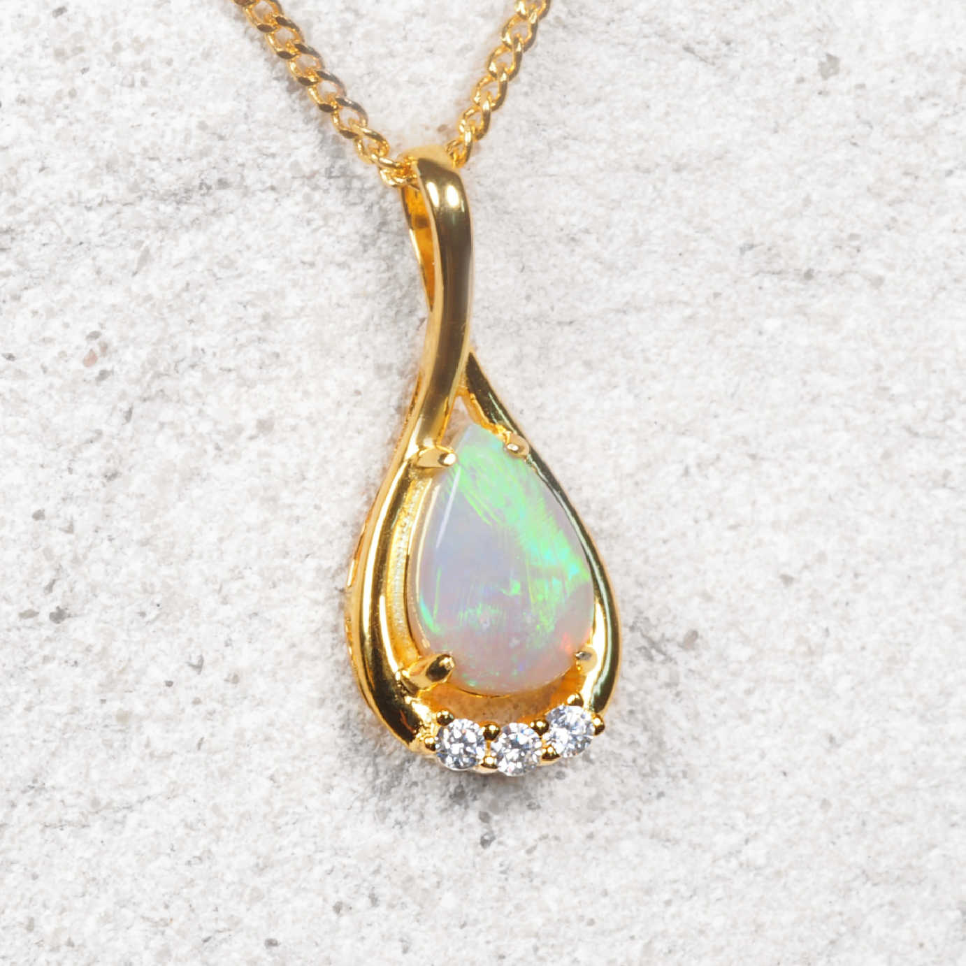 Gold pendant with a teardrop-shaped opal stone on a light gray background