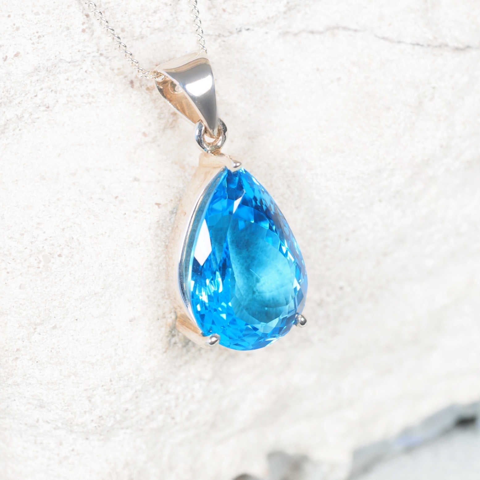 The 'Moana' light Blue Topaz pendant in a claw-style silver bezel, showcasing a faceted teardrop gemstone with bright blue sparkle