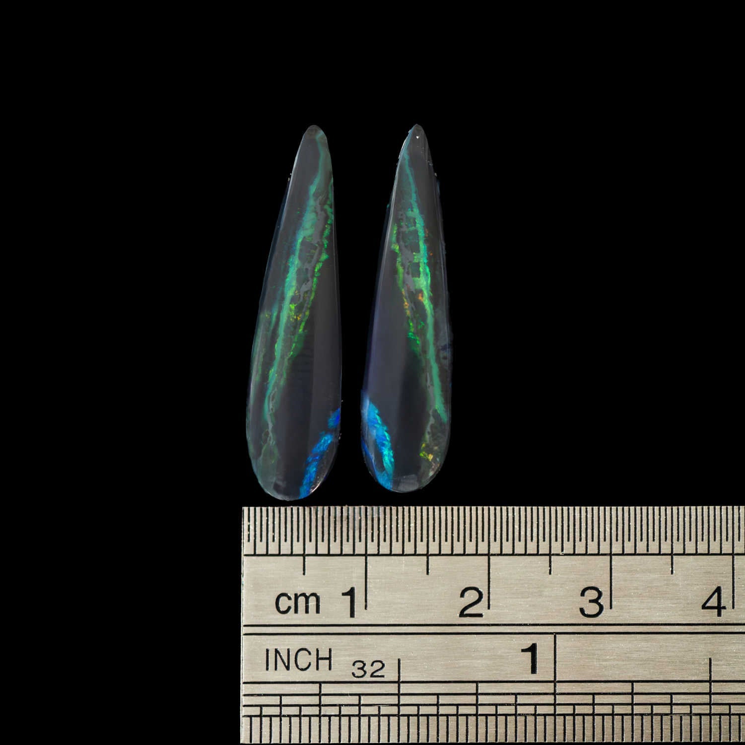 Two iridescent opal stones with a ruler below for scale on a black background