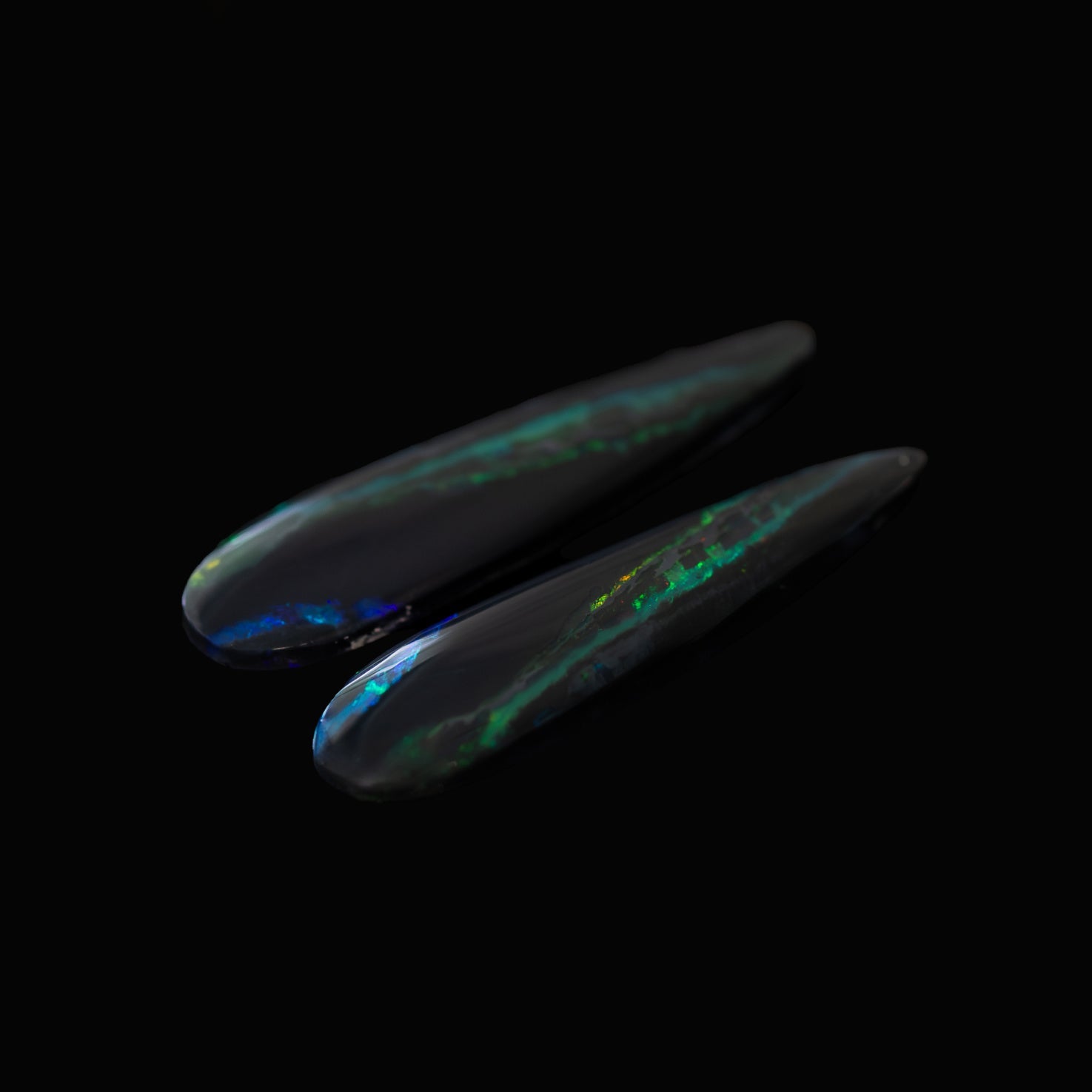 Two glowing Australian black opals on a black background