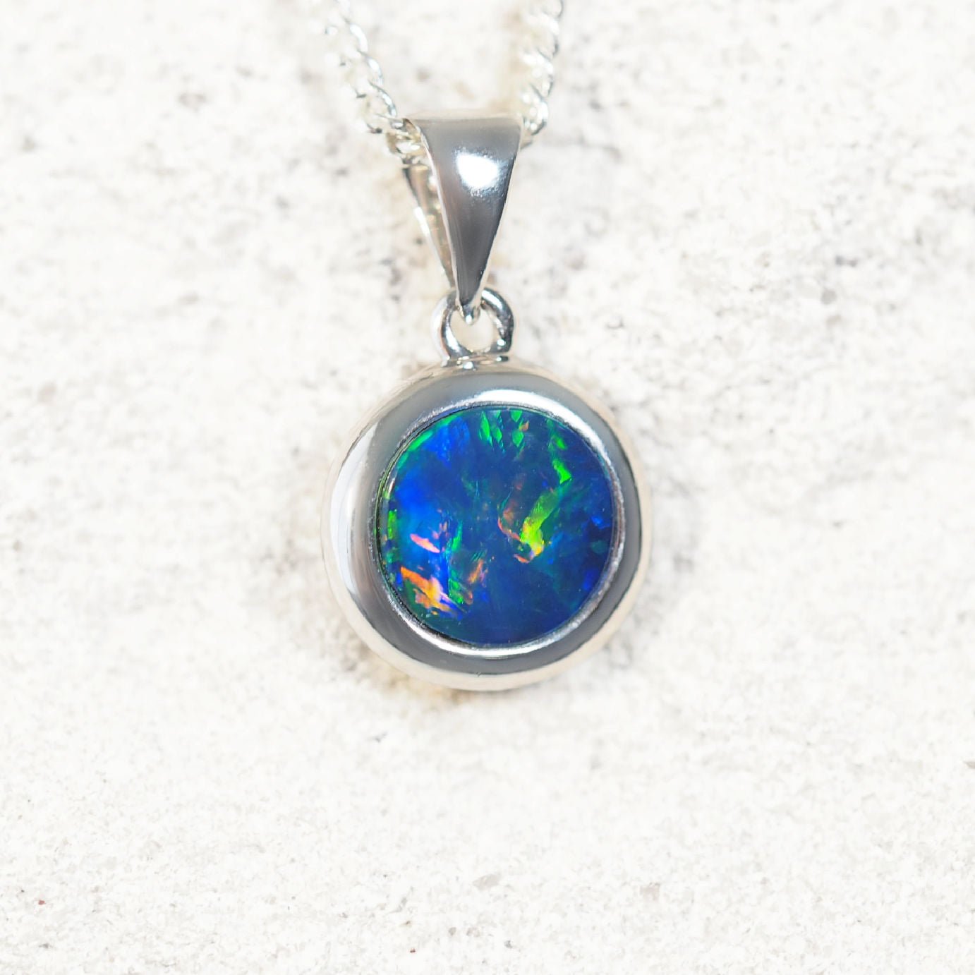 Round Australian doublet opal pendant featuring bright blue base and rainbow colour flashes in white gold setting