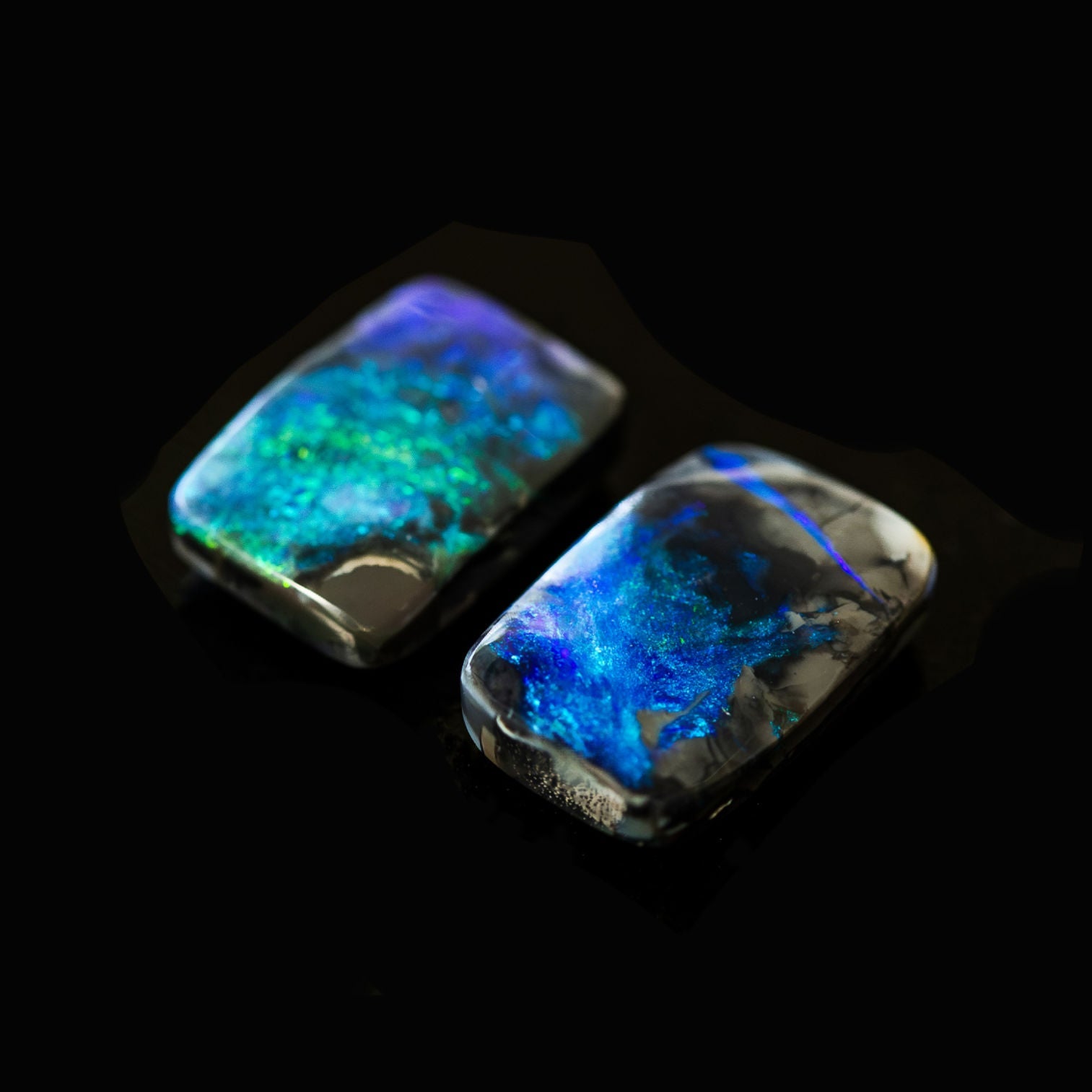 Pair of solid black opals displaying luminous blue and green colour play