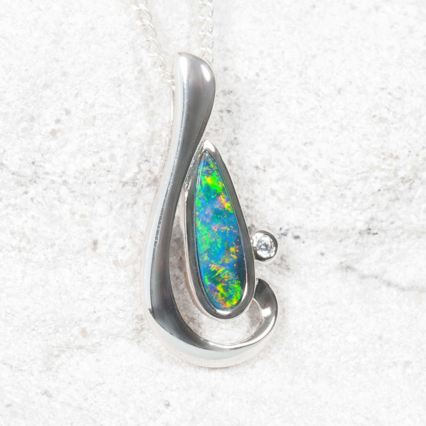 Silver pendant with a colorful opal stone on a textured white background
