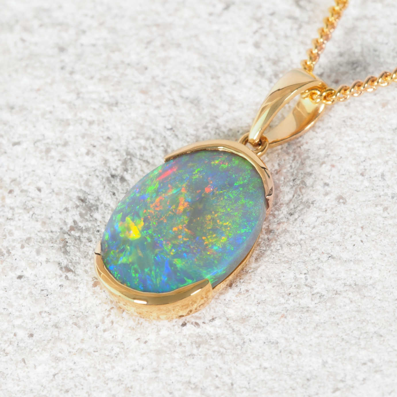 Colourful black Lightning Ridge opal pendant with gold setting on a textured surface