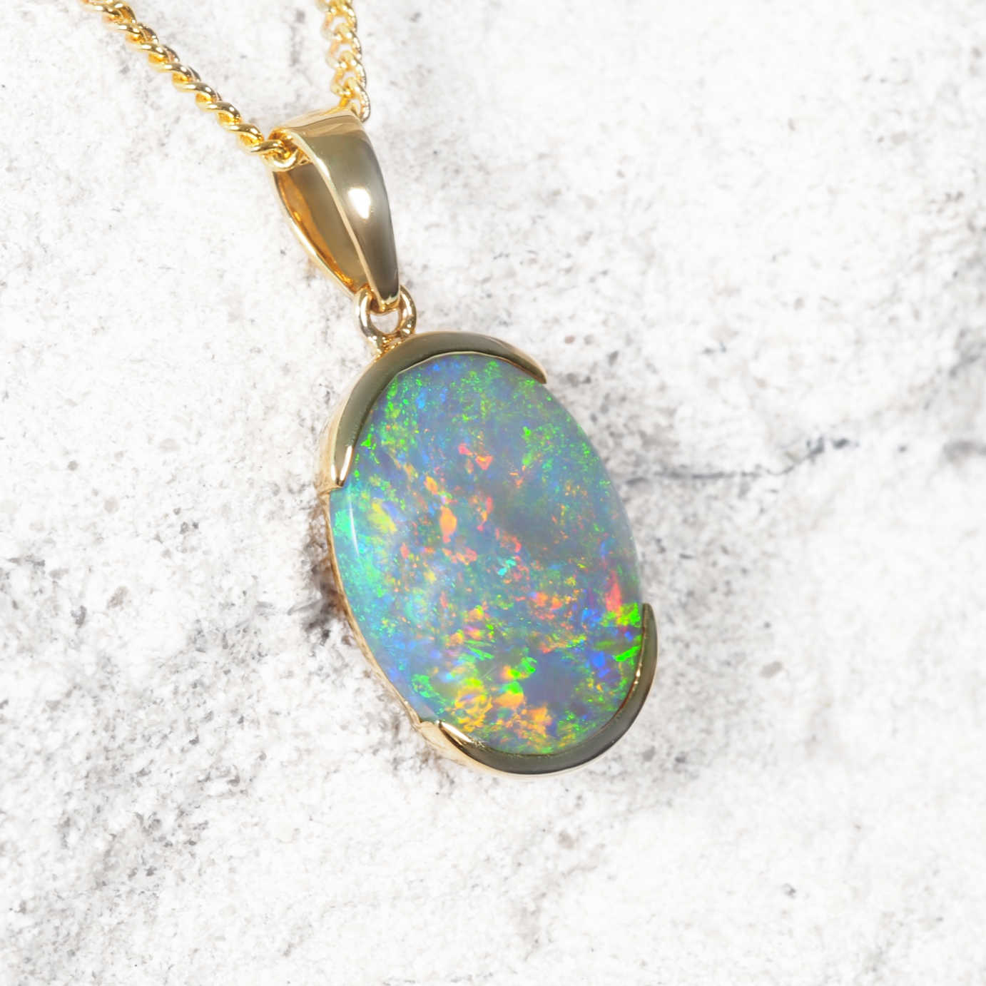 Opal pendant on a gold chain against a marble background