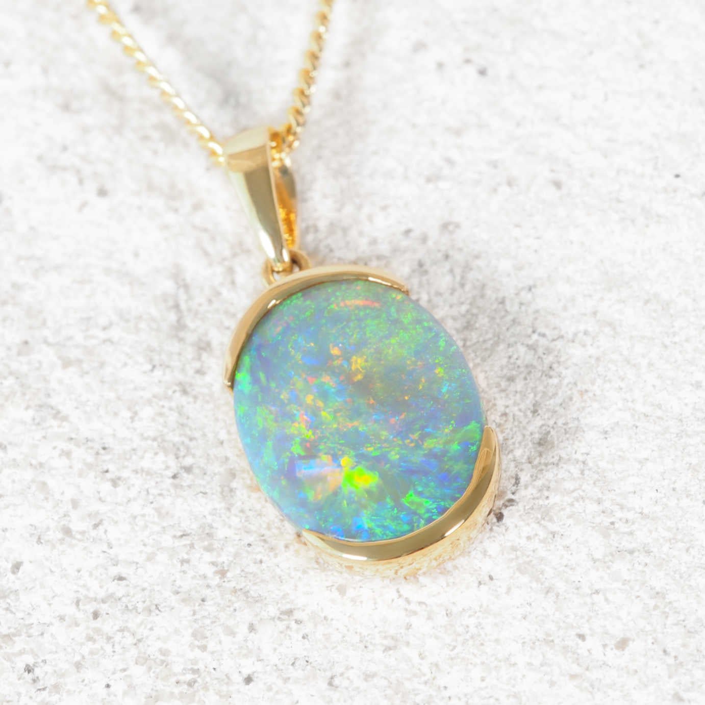 Colourful black opal pendant necklace on a textured white surface