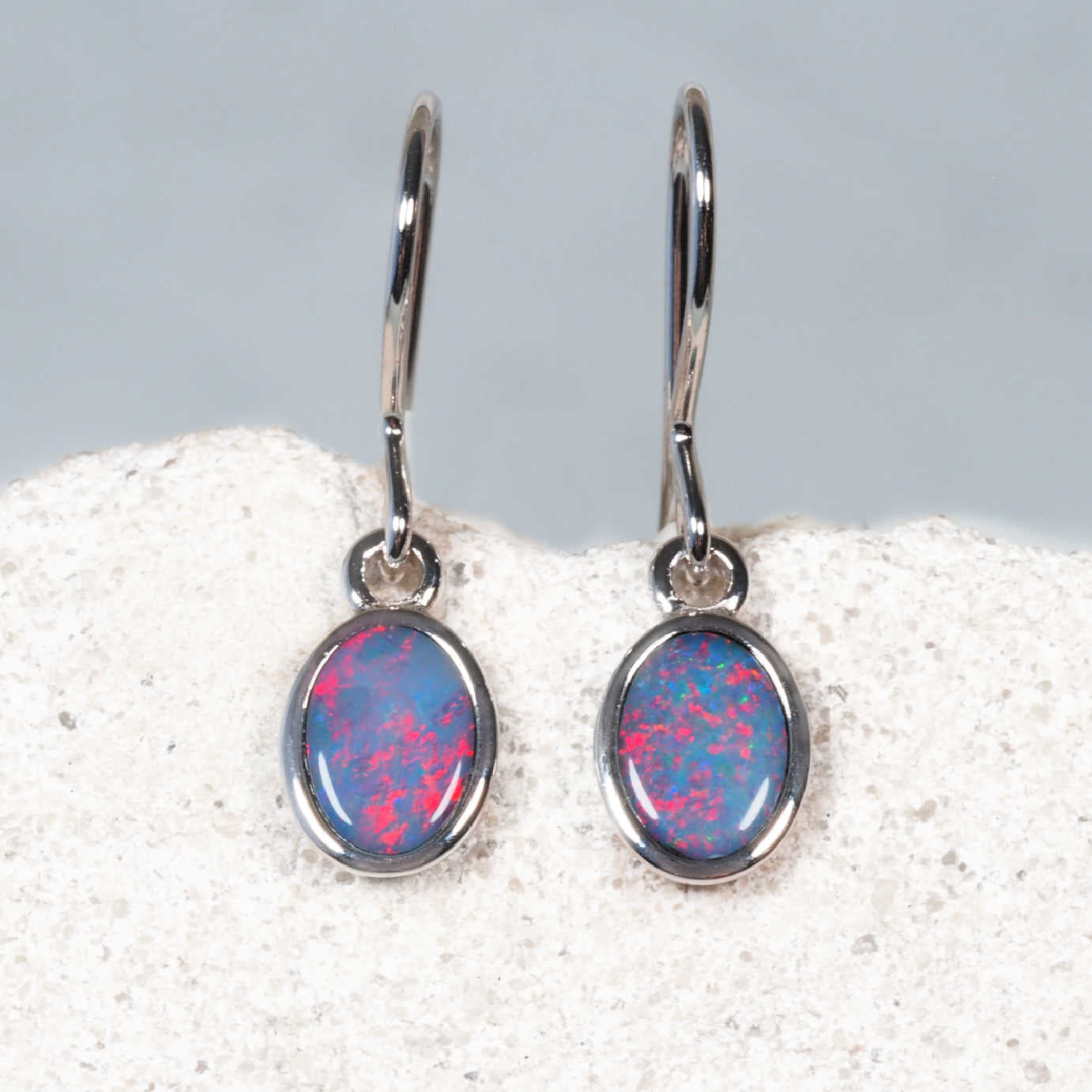 Silver earrings with pink and blue opal stones on a white and gray background