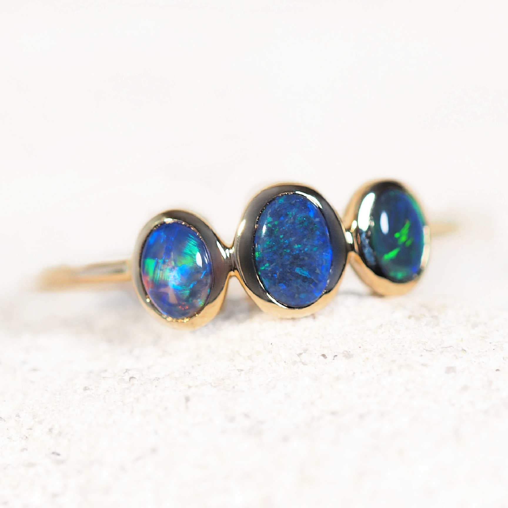 Three oval black opals in 14ct yellow gold setting showing vibrant blue and green