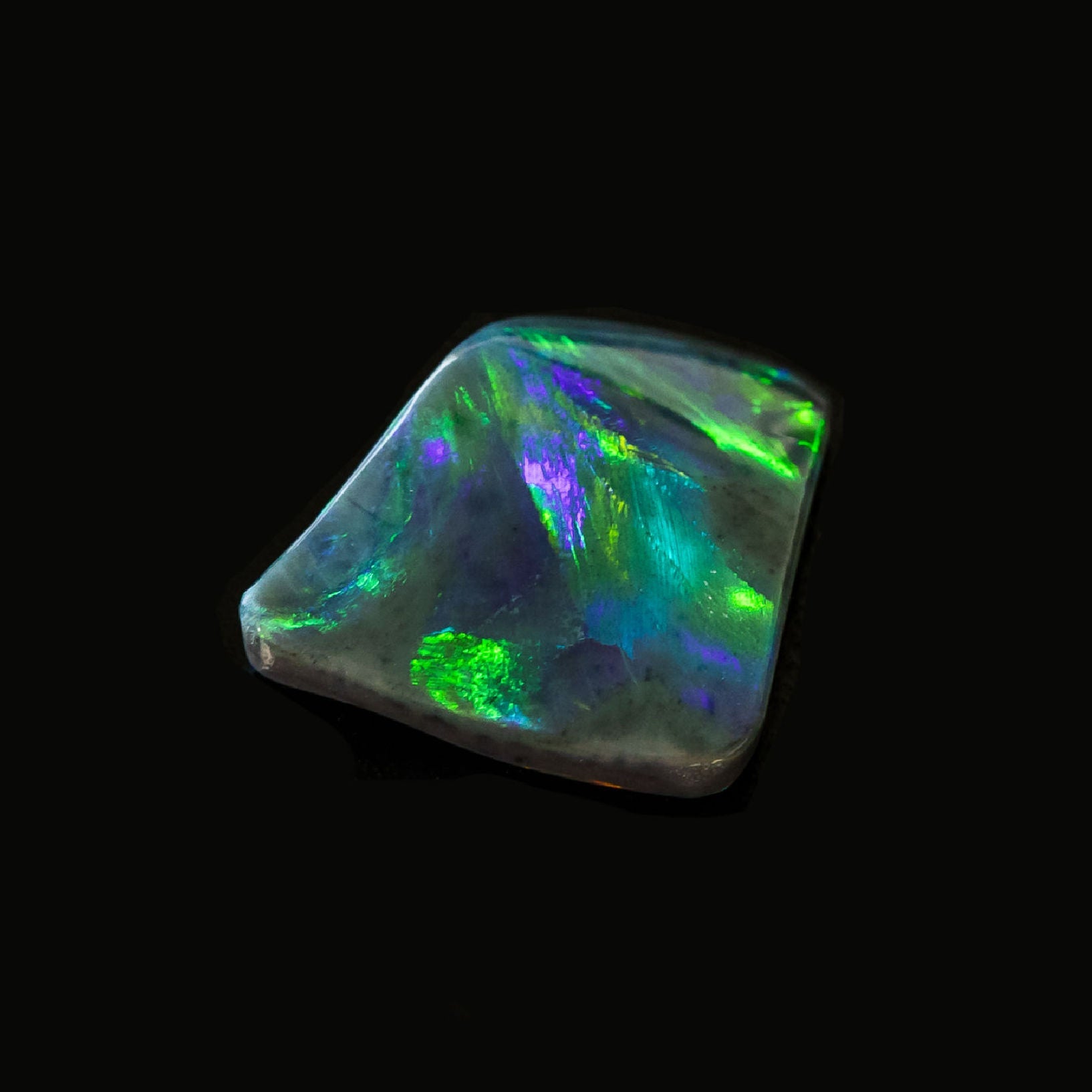 Blue and green solid black opal gemstone, freeform like a stingray in motion