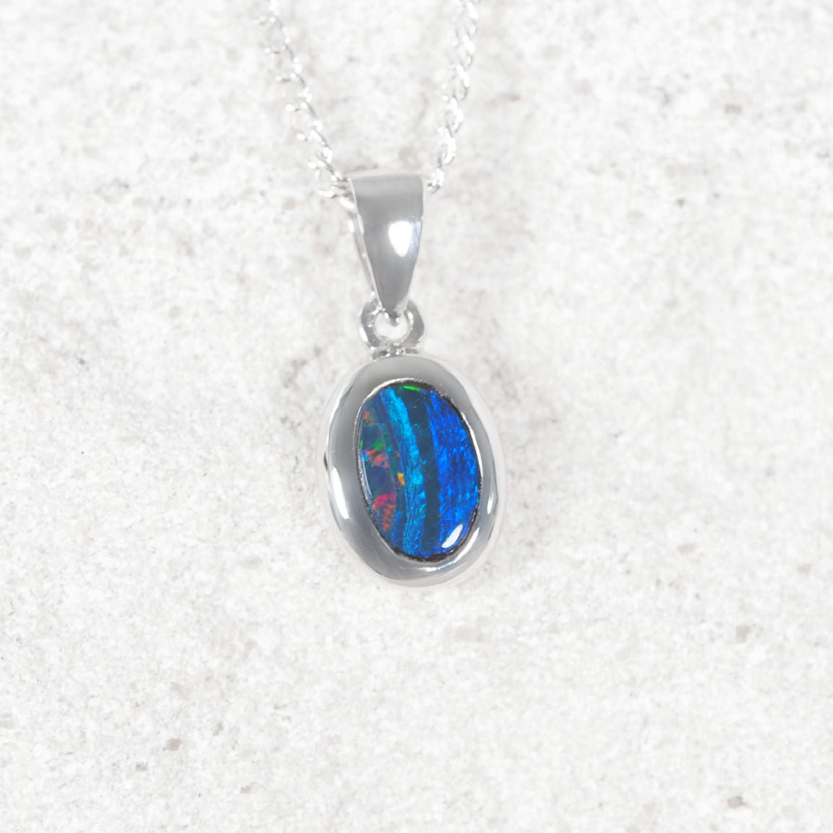 14ct white gold oval pendant necklace featuring a vibrant blue, green, and red iridescent opal stone, suspended from a delicate silver chain against a light textured background.