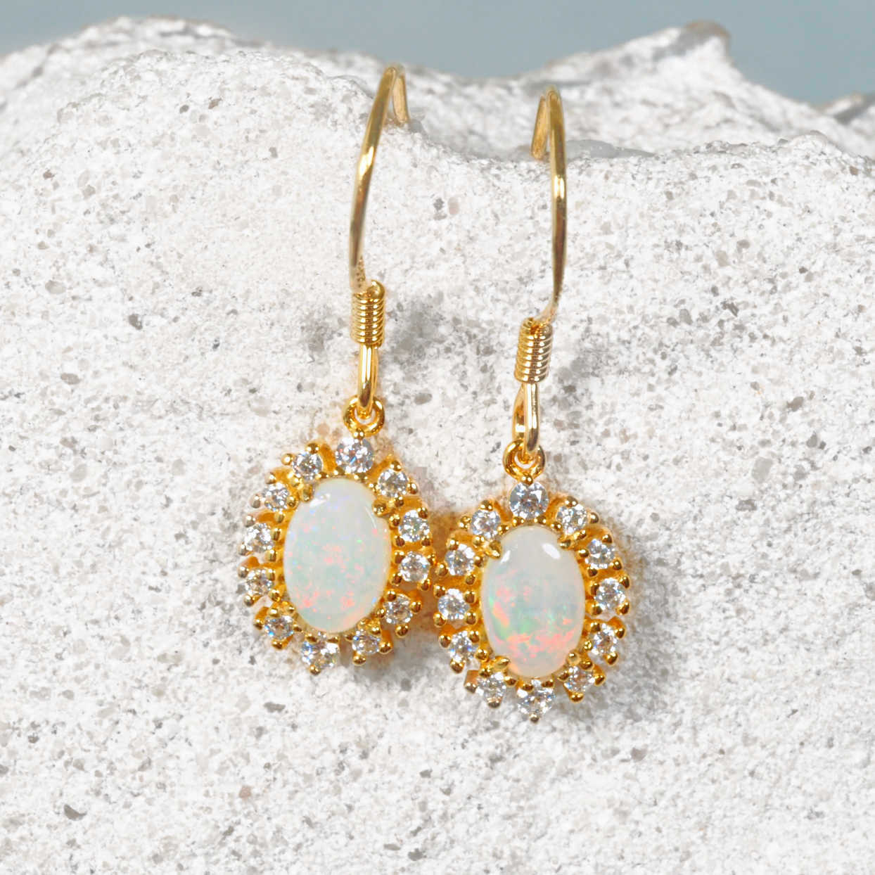 Gold earrings with opal stones on a textured white surface