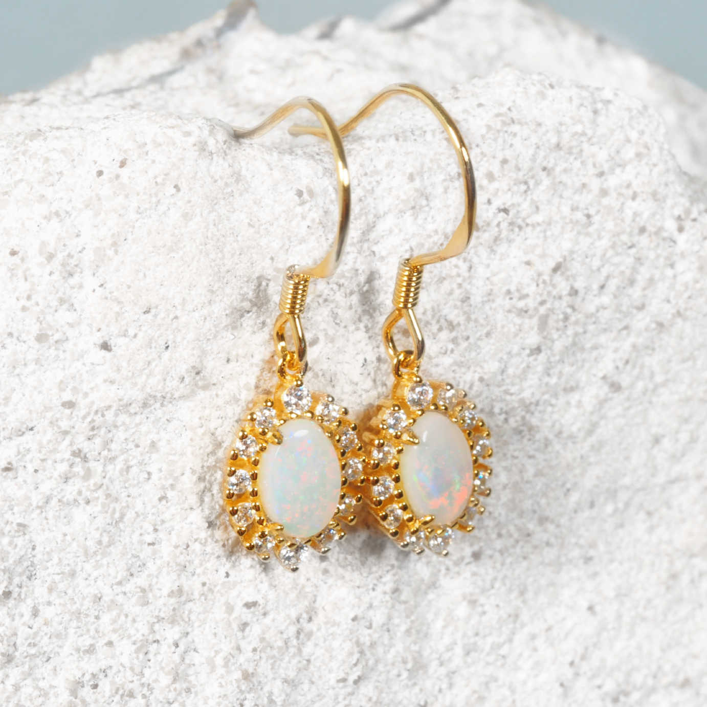 Gold plated silver earrings with colourful opal stones on a textured white surface